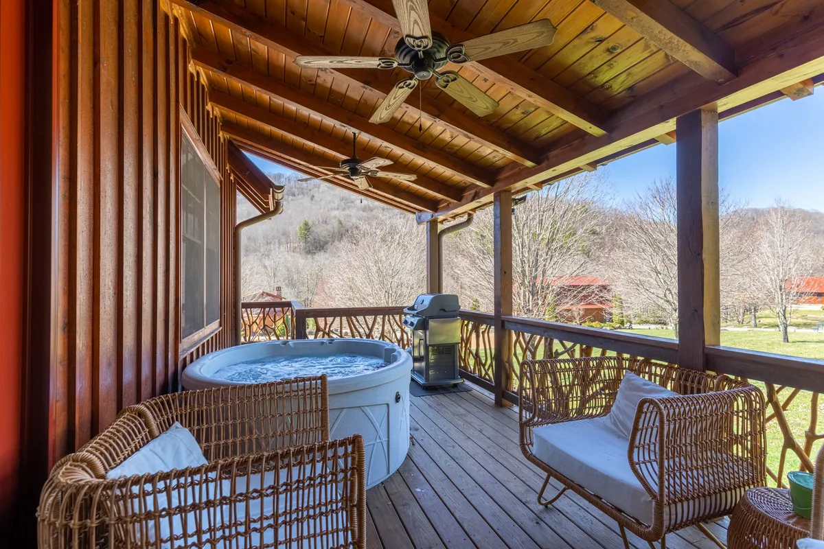 This exterior image highlights a cozy hot tub on the deck, complemented by outdoor seating, a grill, and a wooden ceiling above. The setting is designed for relaxation, with space for socializing or contemplative moments under the open sky.