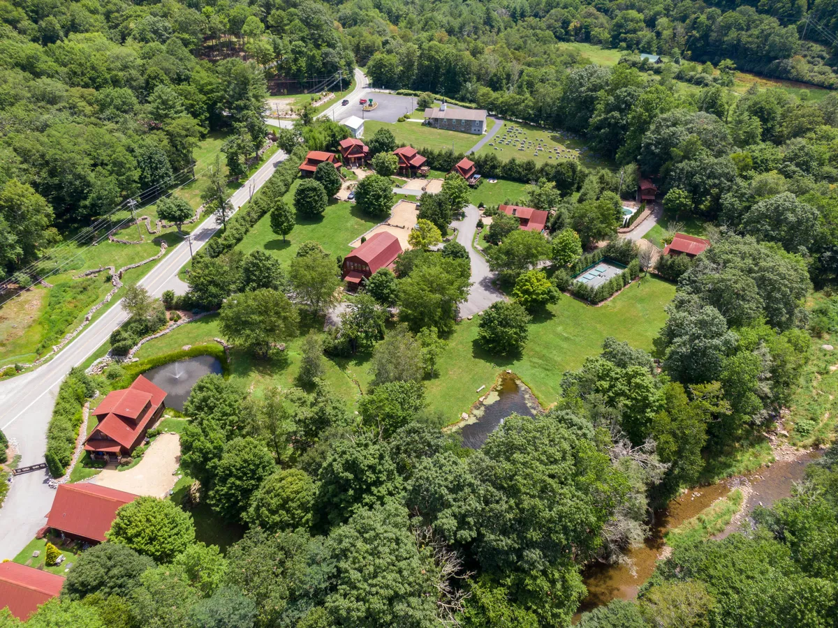 A cluster of red-roofed cabins sits beside a large green lawn and pond, with winding roads and open spaces inviting exploration. The landscape suggests community amenities and plenty of room for outdoor activities.