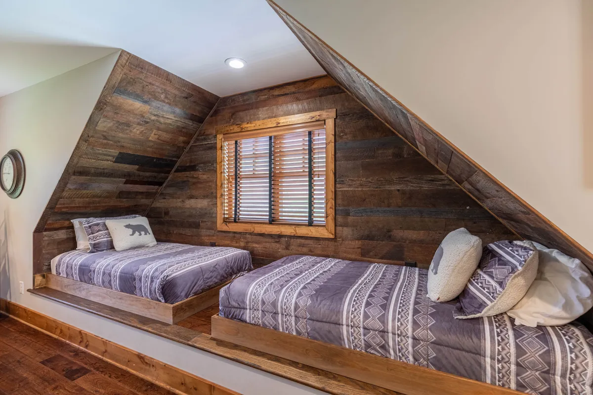 A unique bedroom alcove with twin beds positioned toe-to-toe beneath a window, set against a wooden feature wall and complemented by whimsical bed frames and natural light. Wooden shutters add a rustic charm to the space.