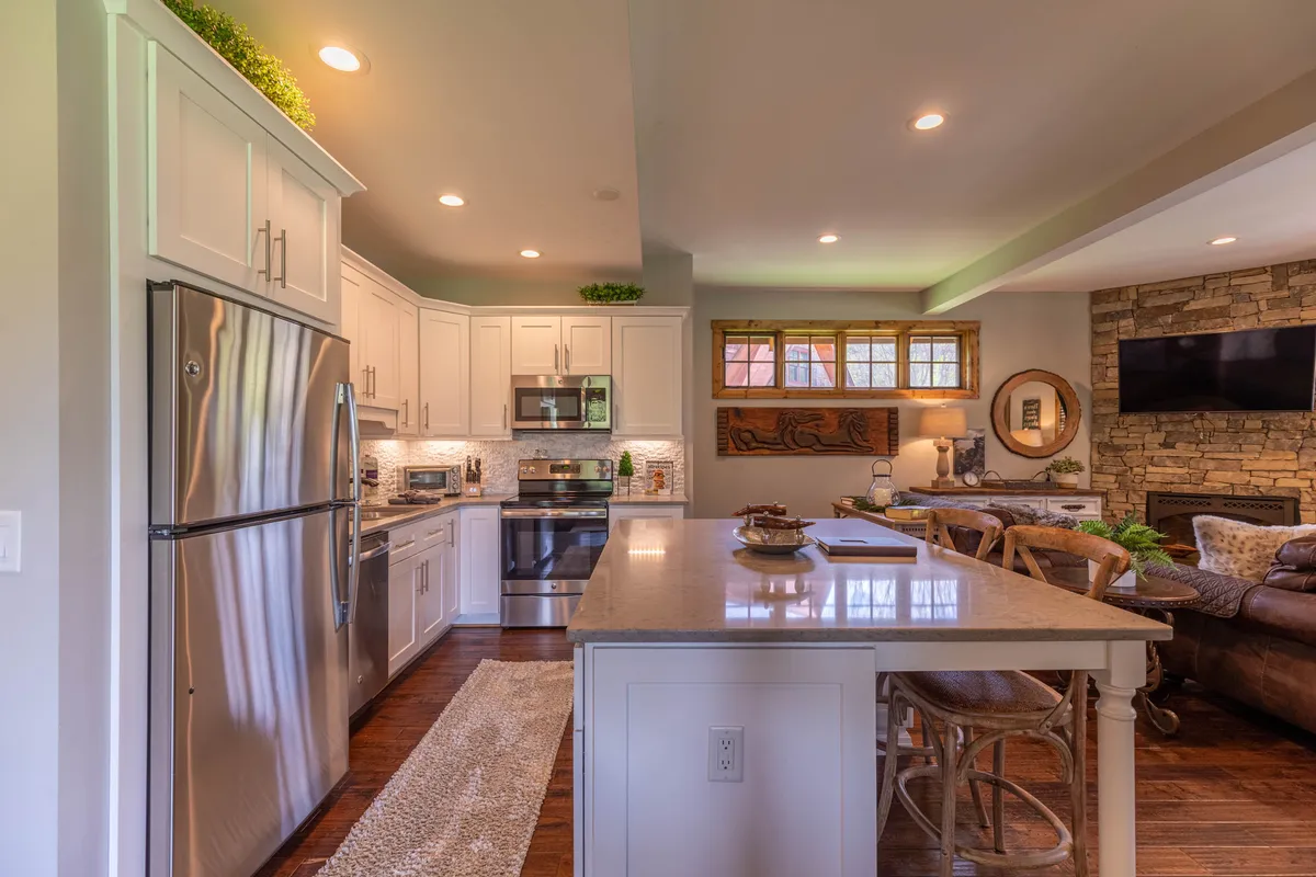 A bright, modern kitchen featuring a central island, stainless steel appliances, granite countertops, and a stone accent wall. Large windows bring in ample natural light, creating a welcoming atmosphere for cooking and socializing.