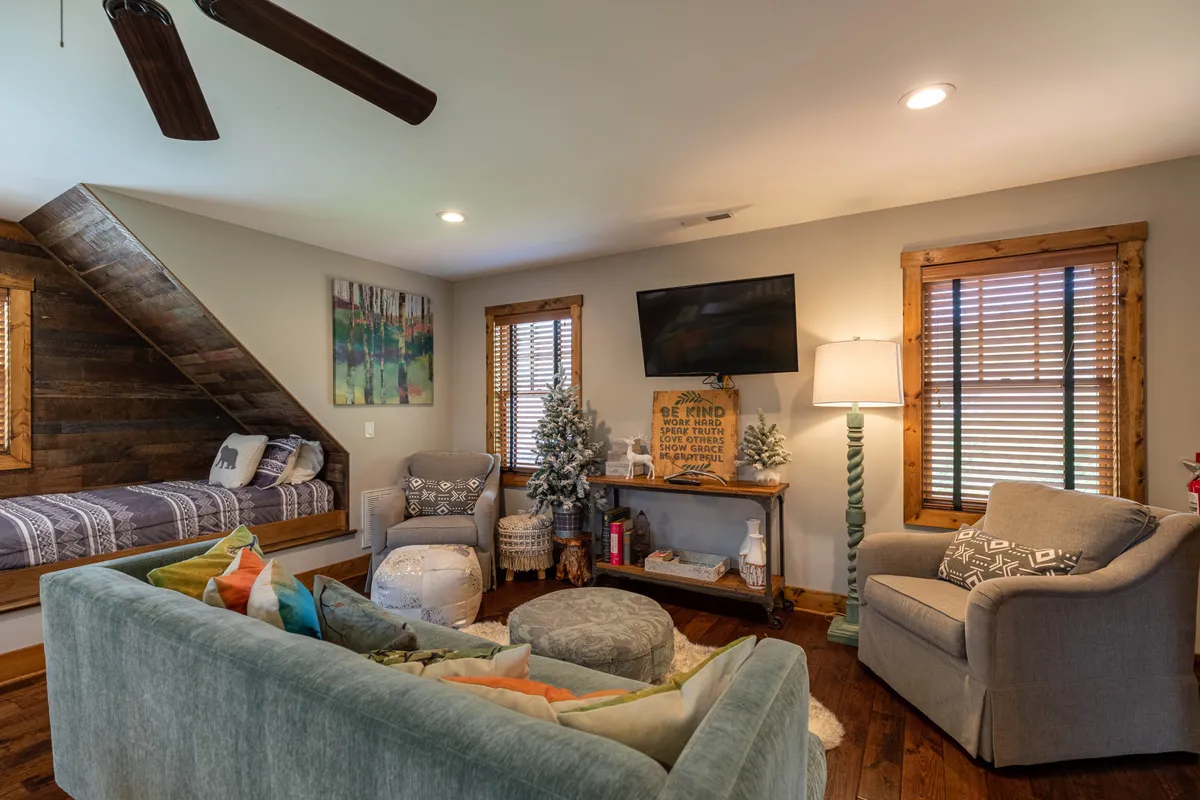 A warm, inviting sitting area with a wooden bed tucked under a sloped ceiling, a sofa adorned with colorful pillows, decorative art on the walls, and a TV mounted above. Potted plants add a touch of greenery to the space, enhancing its welcoming feel.