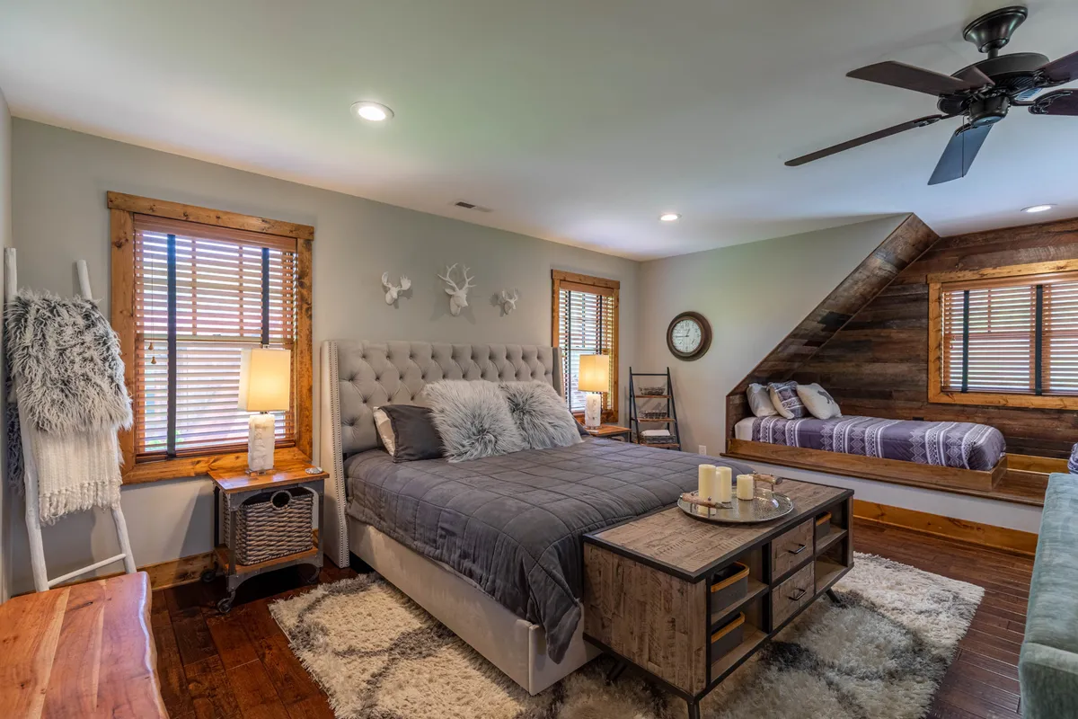 A serene bedroom featuring a king-sized bed with plush bedding, surrounded by wooden furniture and decorative wall accents. Natural light streams in, and a cozy daybed sits nearby, creating a peaceful retreat perfect for relaxing or reading.