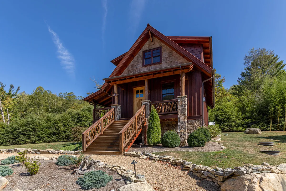 The image showcases the inviting exterior of a single-family cottage, featuring a charming stone facade, a welcoming wooden front door, and a staircase leading up to the entrance. The porch hints at comfortable outdoor seating, perfect for soaking in serene mountain sunsets or gathering around an evening bonfire.