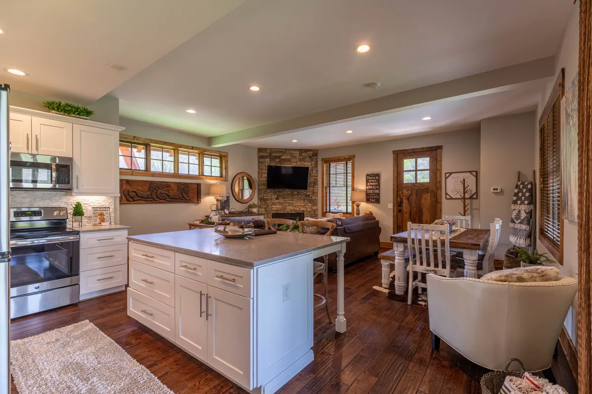 A warm, open interior where the kitchen island flows seamlessly into a dining area with a table for four and a cozy lounge anchored by a stone fireplace. The combined spaces are perfect for group gatherings, meals, and relaxation.